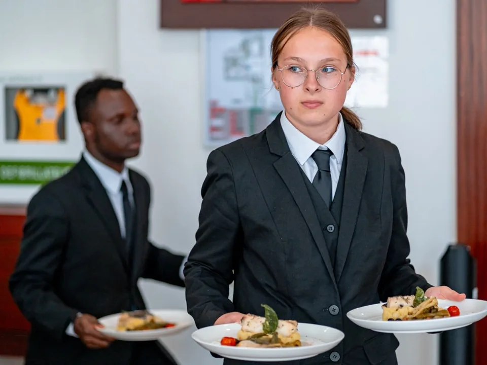 Apprentie en salle portant deux assiettes au restaurant d’application